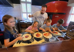 Czterej uczniowie smarują placki pastą pomidorową.