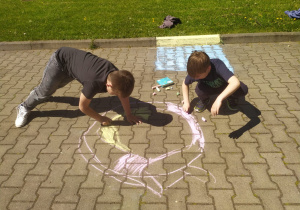 Dwóch chłopców maluje kredą na chodniku