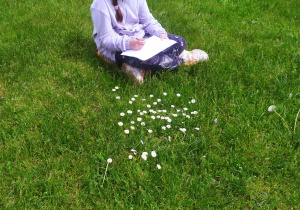 Dziewczynka siedzi na trawie i maluje