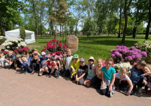 Zbiorowe zdjęcie uczniów przed pomnikiem na tle rododendronów