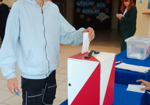 Uczeń wrzuca kartę do urny wyborczej