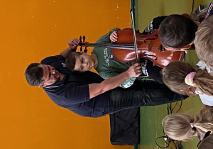 Uczeń z pomocą muzyka gra na wiolonczeli.