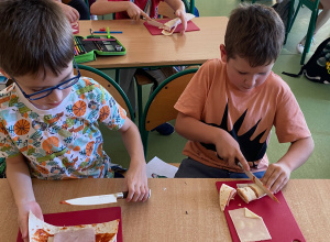 Uczniowie na czerwonych deskach kroją tortlillę.