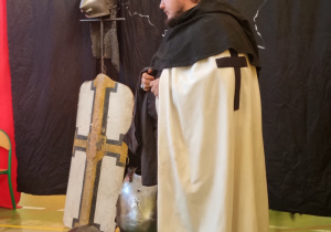 Mężczyzna prezentuje płaszcz zakonu Krzyżackiego.