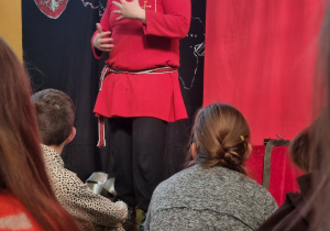 Brodaty mężczyzna ubrany w czerwony kubrak opowiada dzieciom historie.