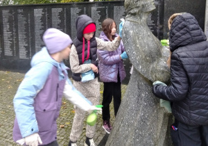 Uczniowie czyszczą pomnik.