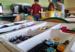 Klocki LEGO posortowane według funkcji leżą w kuwetkach na ławkach szkolnych.