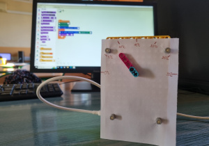 Prosty termometr wskazówkowy z klocków LEGO, w tle monitor z kodem programu.