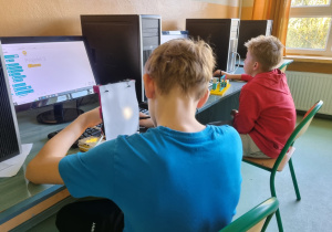 Dwóch chłopców siedzi przed komputerami i buduje urządzenia z klocków LEGO.