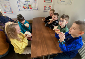 Uczniowie siedzą przy stole i jedzą chleb z masłem.