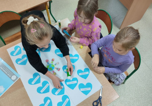 Trzy dziewczynki przyklejają serca na plakacie