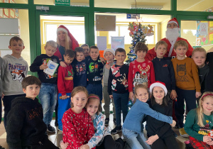 Zbiorowe zdjęcie uczniów z Mikołajem na szkolnym korytarzu.