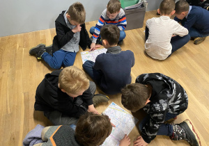 Uczniowie siedzą na podłodze w podgrupach i zaznaczają na mapach obiekty.