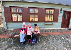 Trzy dziewczynki siedzą przed zabytkowym drewnianym domem.