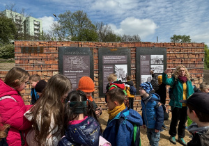 Uczniowie stoją przed pamiątkowymi tablicami w parku.