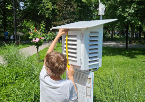 Uczeń mierzy drzwi stacji meteorologicznej.