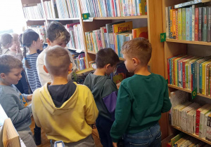 Uczniowie stoją przy regałach z książkami i oglądają je