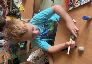 Chłopiec w niebieskiej koszulce maluje kamień.