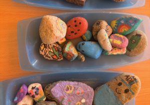 Pomalowane kamienie leżą na niebieskich tacach.