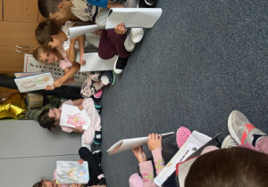 Uczniowie siedzą na dywanie i prezentują swoje rysunki 1