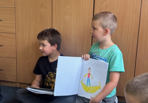 Uczeń w zielonej koszulce pokazuje swój obrazek kolegom.