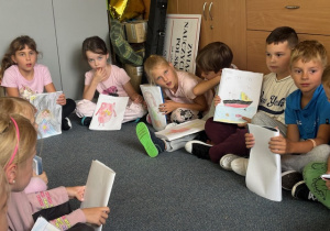 Uczniowie siedzą na dywanie i prezentują swoje rysunki 2
