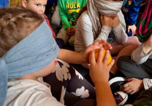 Uczeń z zawiązanymi oczami próbuje różnymi innymi zmysłami zgadnąć, jaki ma owoc.