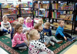 Dzieci siedzą na dywanie w bibliotece szkolnej.