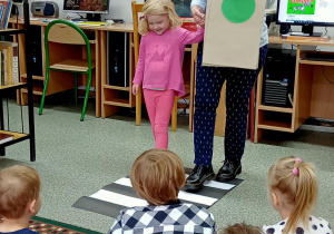 Dzieci siedzą na dywanie i patrzą, jak bibliotekarka pokazuje zielone światło.