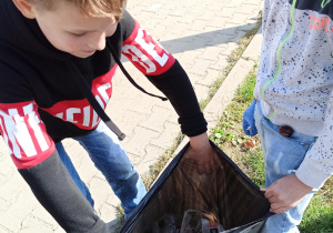Uczniowie wkładają śmieci do worka.