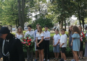 Uczniowie wręczają kwiaty pod tablicą pamiątkową upamiętniającą mieszkańców Konstantynowia Łódzkiego zamordowanych podczas II wojny światowej.