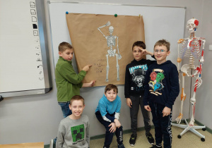 pięciu chłopców na tle wykonanego plakatu o układzie szkieletowym