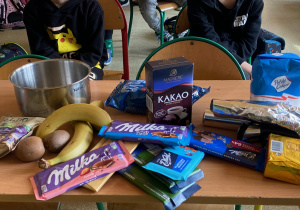Na ławce są prezentowane różne rodzaje czekolad i składniki potrzebne do jej przygotowania