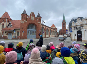 Uczniowie stoją przed bramą do hali targowej, na której widnieje herb Bydgoszczy