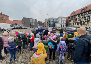 Uczniowie stoją na Starym Rynku i słuchają przewodnika.